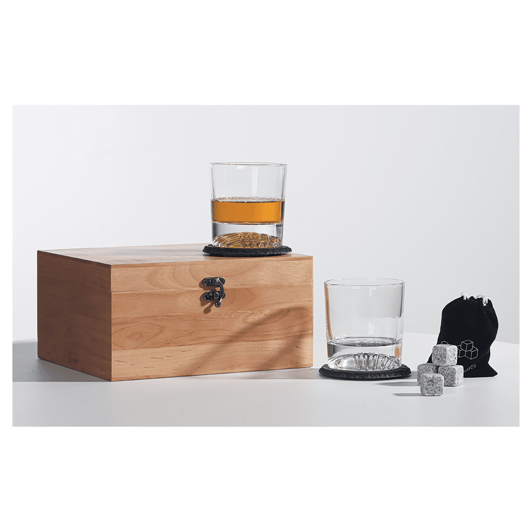 Wooden box with a glass of whiskey, another glass, and a black pouch on a white surface.