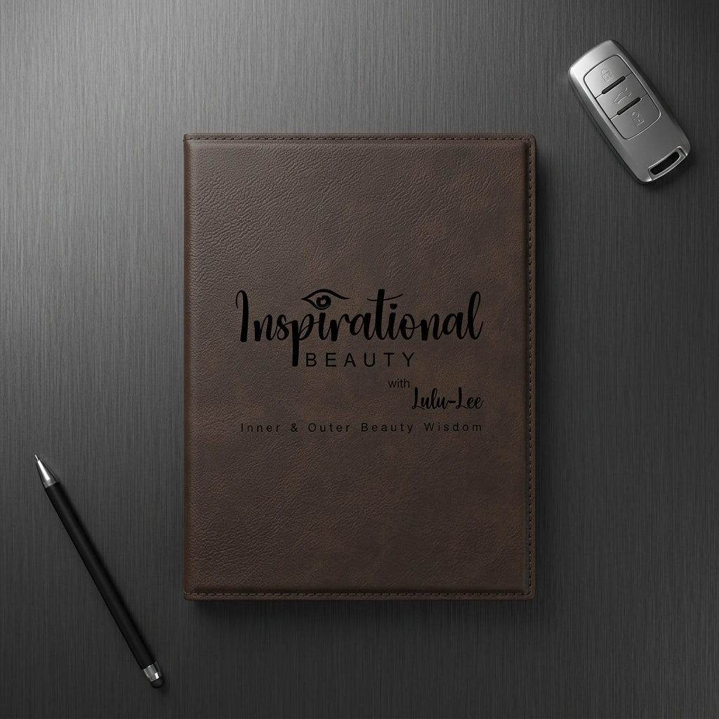 Brown leather notebook with 'Inspirational Beauty' text on a dark surface with a pen and car key.